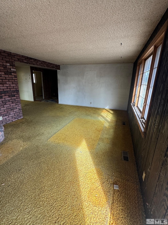 spare room with brick wall, carpet, and a textured ceiling