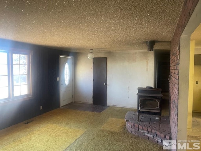 unfurnished living room with carpet, a textured ceiling, and a wood stove