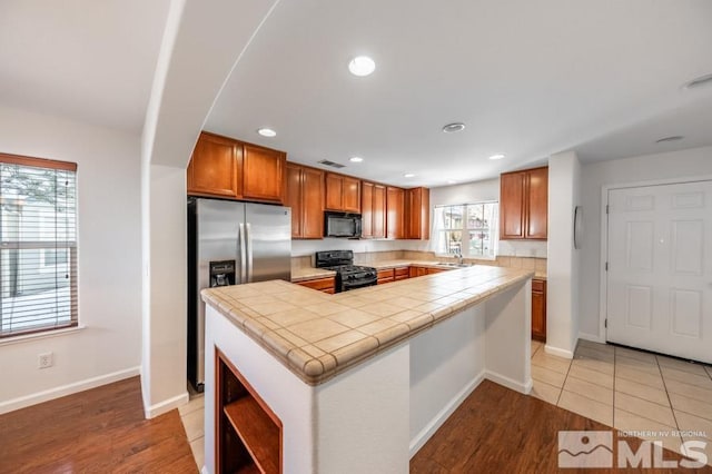 kitchen featuring sink, a center island, tile counters, black appliances, and light hardwood / wood-style floors