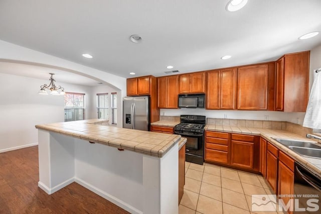 kitchen with tile countertops, decorative light fixtures, sink, and black appliances