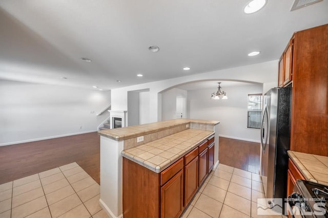 kitchen with pendant lighting, light wood-type flooring, tile counters, and stainless steel refrigerator