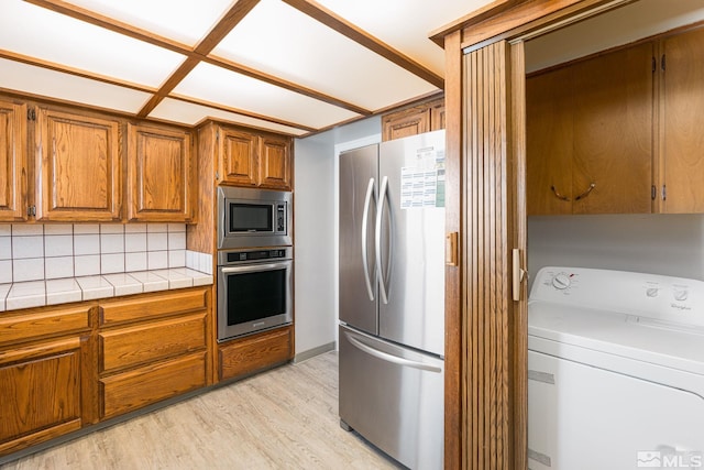 kitchen with appliances with stainless steel finishes, tile countertops, washer / clothes dryer, decorative backsplash, and light hardwood / wood-style flooring