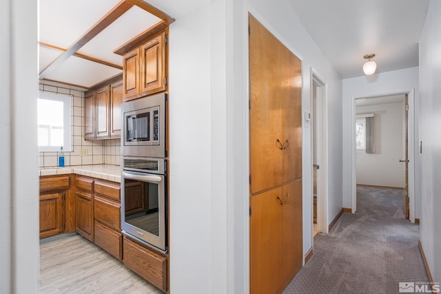 kitchen featuring stainless steel appliances, tasteful backsplash, light carpet, and tile countertops