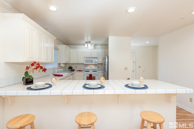 kitchen featuring white appliances, a kitchen bar, tile countertops, and kitchen peninsula