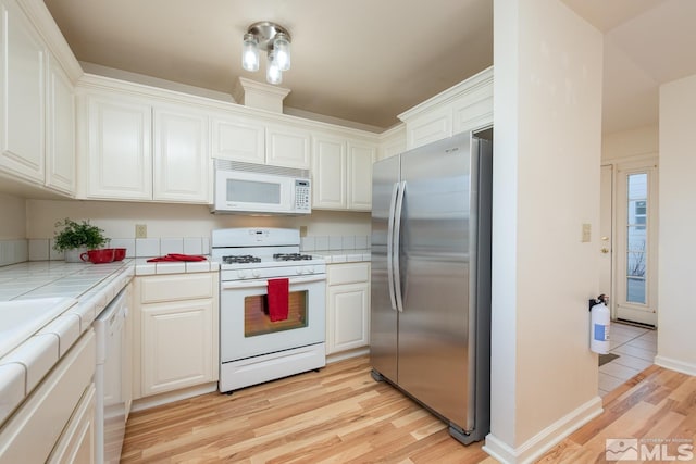 kitchen with white cabinetry, white appliances, tile countertops, and light hardwood / wood-style flooring