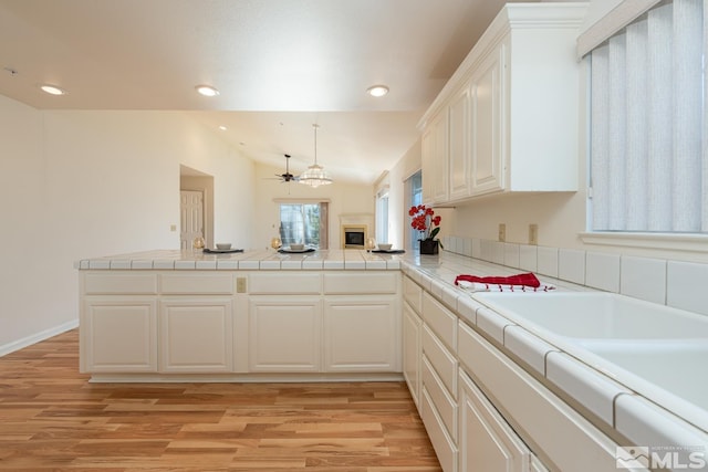 kitchen featuring tile counters, kitchen peninsula, vaulted ceiling, and light hardwood / wood-style flooring