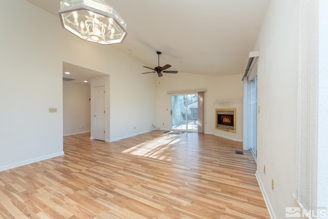 unfurnished living room with high vaulted ceiling, ceiling fan with notable chandelier, and light wood-type flooring