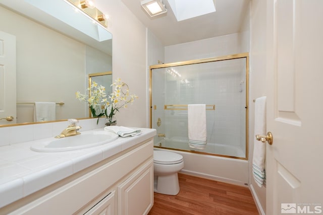 full bathroom with toilet, wood-type flooring, bath / shower combo with glass door, a skylight, and vanity