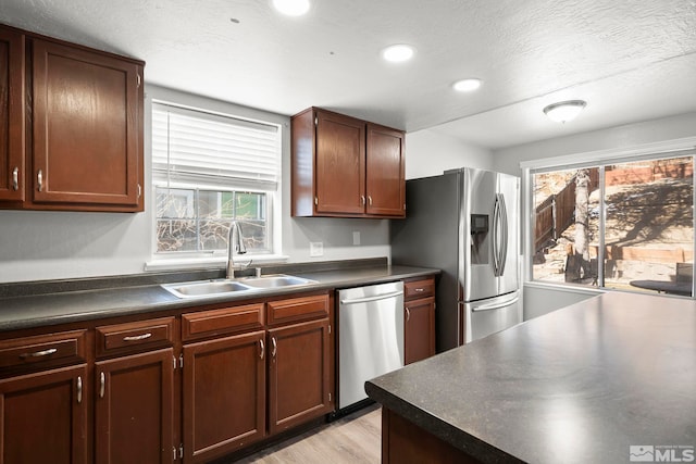 kitchen with appliances with stainless steel finishes, sink, a textured ceiling, and light hardwood / wood-style flooring