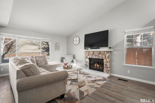 living room with hardwood / wood-style flooring, vaulted ceiling, and a stone fireplace