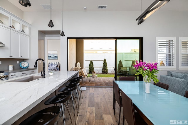 kitchen with sink, white cabinetry, hanging light fixtures, light stone counters, and a healthy amount of sunlight