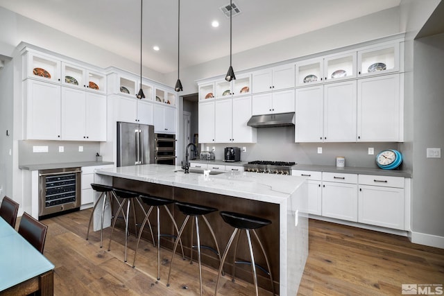 kitchen with sink, a center island with sink, pendant lighting, stainless steel appliances, and beverage cooler