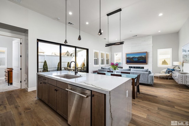 kitchen with sink, a kitchen island with sink, light stone countertops, dark hardwood / wood-style flooring, and stainless steel dishwasher