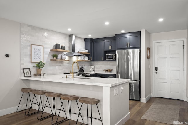 kitchen with appliances with stainless steel finishes, wall chimney exhaust hood, a breakfast bar, and kitchen peninsula