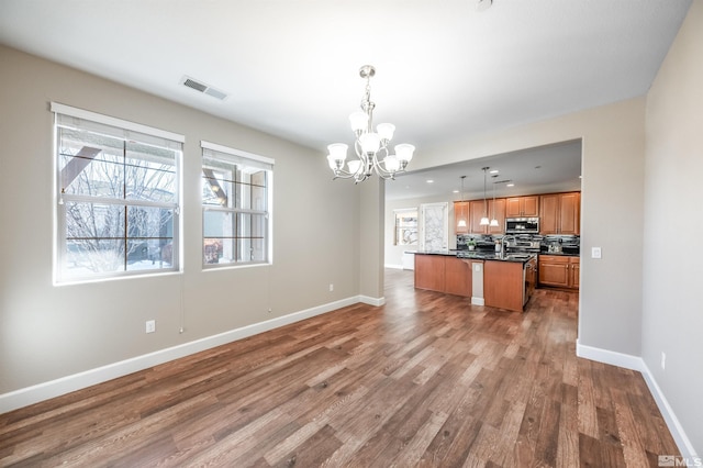 kitchen featuring pendant lighting, hardwood / wood-style flooring, an inviting chandelier, a center island, and decorative backsplash