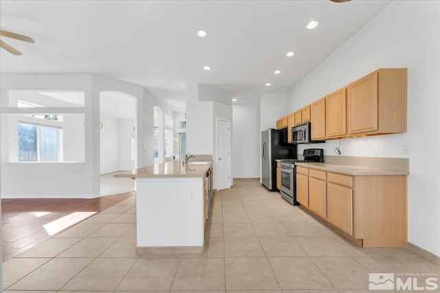 kitchen with sink, a center island with sink, light brown cabinets, ceiling fan, and stainless steel appliances