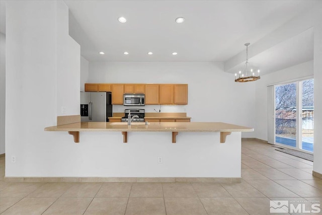 kitchen featuring light tile patterned flooring, a breakfast bar area, appliances with stainless steel finishes, kitchen peninsula, and pendant lighting