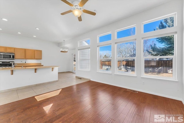 kitchen with a breakfast bar area, light hardwood / wood-style flooring, appliances with stainless steel finishes, pendant lighting, and ceiling fan with notable chandelier