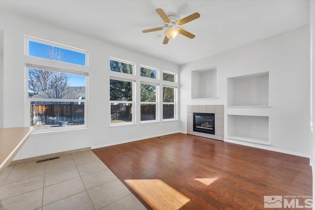 unfurnished living room with hardwood / wood-style flooring, ceiling fan, a healthy amount of sunlight, and a tile fireplace