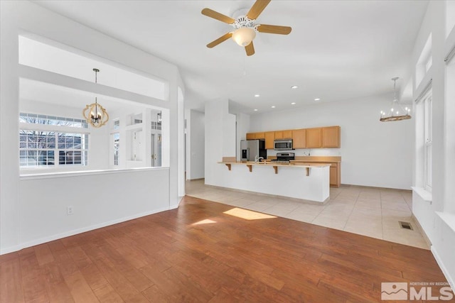 unfurnished living room with ceiling fan with notable chandelier and light hardwood / wood-style floors