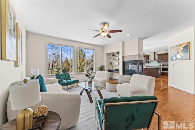 living room featuring wood-type flooring, ceiling fan, and a multi sided fireplace