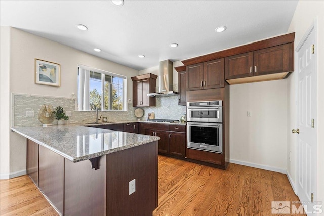 kitchen featuring sink, a breakfast bar, light stone counters, kitchen peninsula, and wall chimney exhaust hood