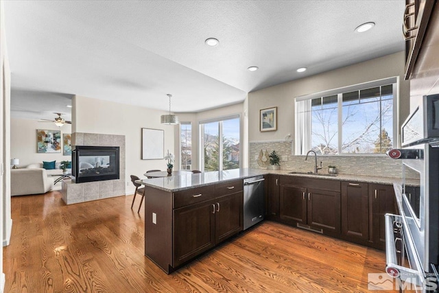 kitchen with pendant lighting, sink, light stone countertops, stainless steel dishwasher, and kitchen peninsula