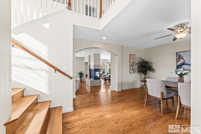 entrance foyer with ceiling fan, wood-type flooring, a multi sided fireplace, and a towering ceiling