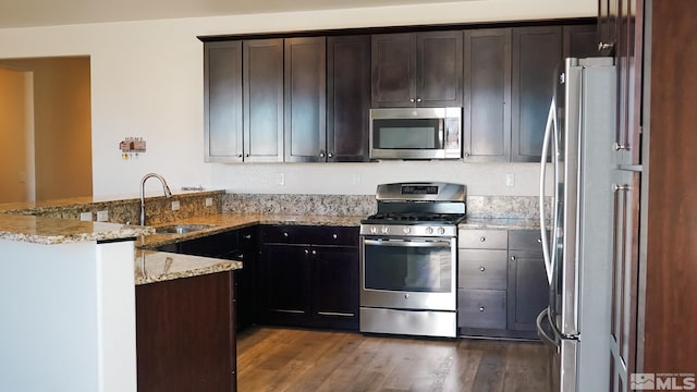 kitchen featuring appliances with stainless steel finishes, sink, light stone counters, kitchen peninsula, and dark wood-type flooring