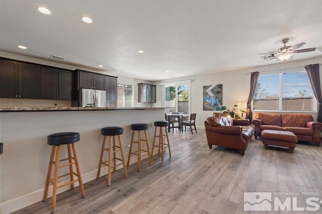 kitchen featuring stainless steel refrigerator, a kitchen bar, light stone counters, dark brown cabinets, and light hardwood / wood-style flooring