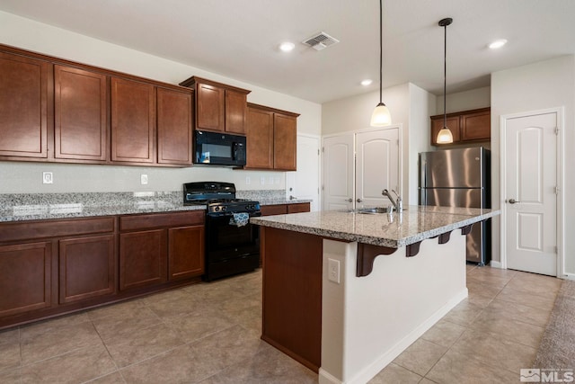 kitchen featuring hanging light fixtures, a center island with sink, a kitchen breakfast bar, light stone countertops, and black appliances