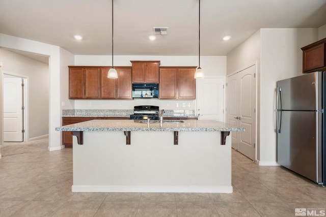 kitchen with a breakfast bar area, stainless steel refrigerator, stove, hanging light fixtures, and an island with sink