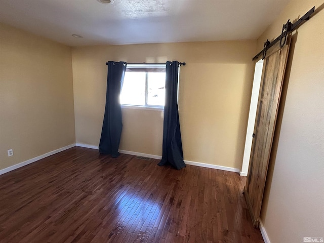 unfurnished room with a barn door and dark hardwood / wood-style flooring