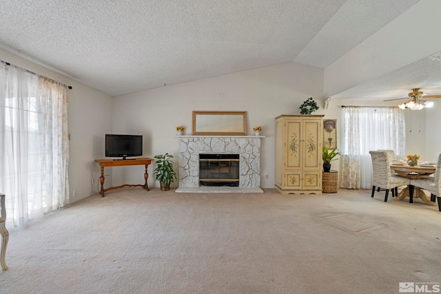 unfurnished living room featuring lofted ceiling, ceiling fan, a fireplace, a textured ceiling, and light colored carpet