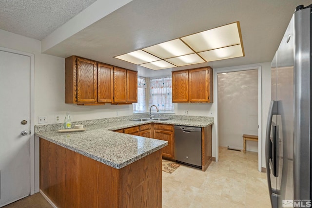 kitchen featuring sink, appliances with stainless steel finishes, light stone counters, a textured ceiling, and kitchen peninsula