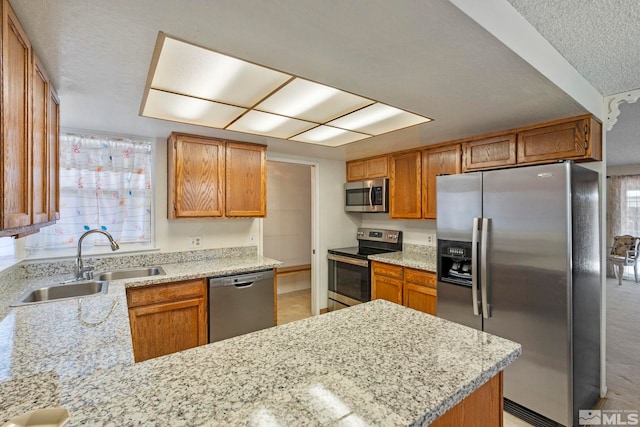 kitchen featuring sink, plenty of natural light, stainless steel appliances, light stone countertops, and kitchen peninsula