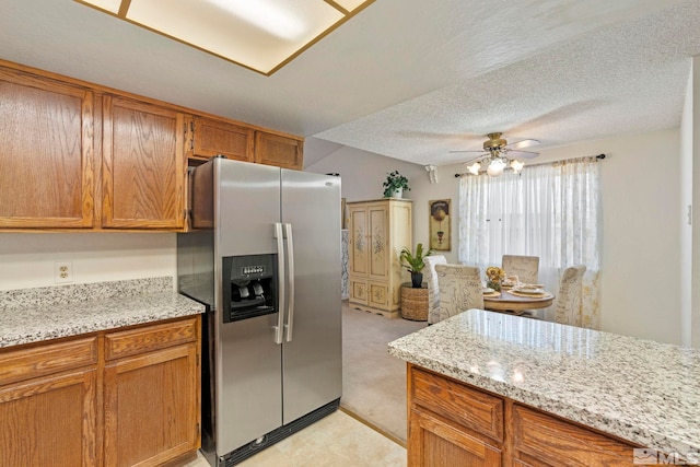 kitchen featuring stainless steel refrigerator with ice dispenser, ceiling fan, light stone countertops, and a textured ceiling