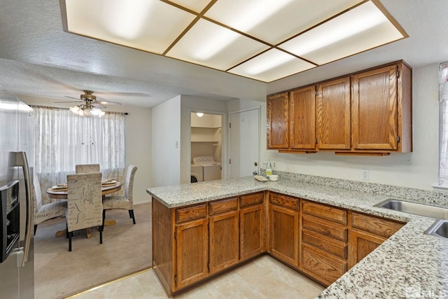 kitchen with independent washer and dryer, light carpet, kitchen peninsula, ceiling fan, and light stone countertops