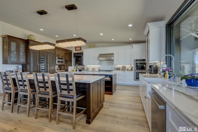 kitchen featuring a breakfast bar, decorative light fixtures, stainless steel appliances, a kitchen island with sink, and white cabinets