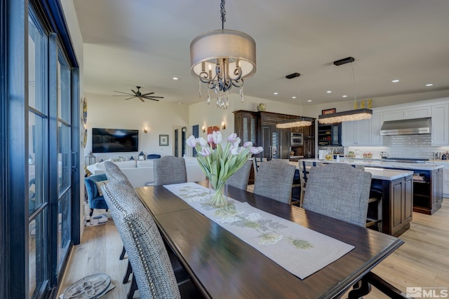 dining area with ceiling fan with notable chandelier and light hardwood / wood-style floors