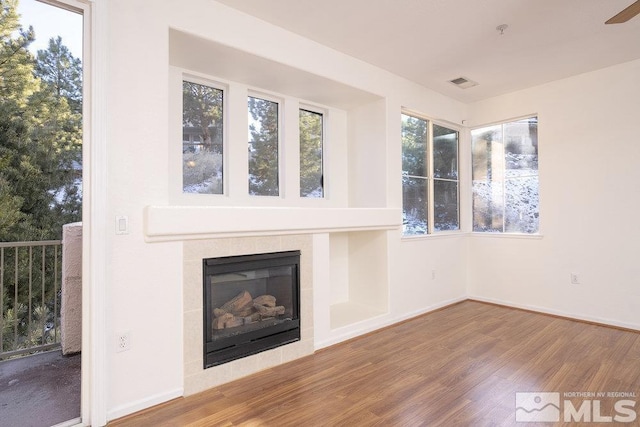 unfurnished living room with a fireplace, wood finished floors, visible vents, and baseboards