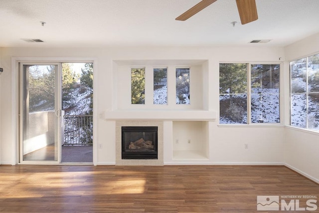 unfurnished living room with ceiling fan, wood-type flooring, and a tiled fireplace