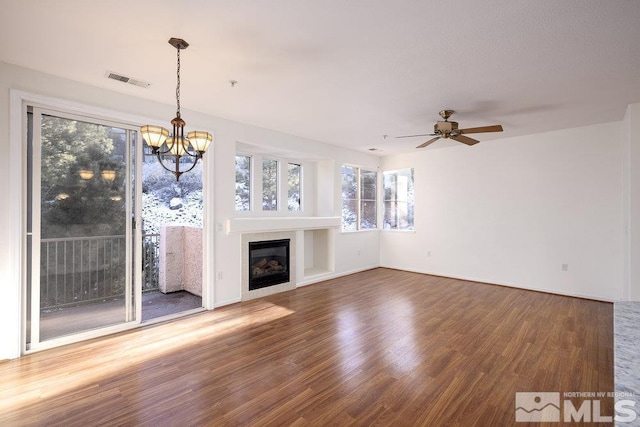 unfurnished living room featuring wood finished floors, baseboards, visible vents, a tile fireplace, and ceiling fan with notable chandelier