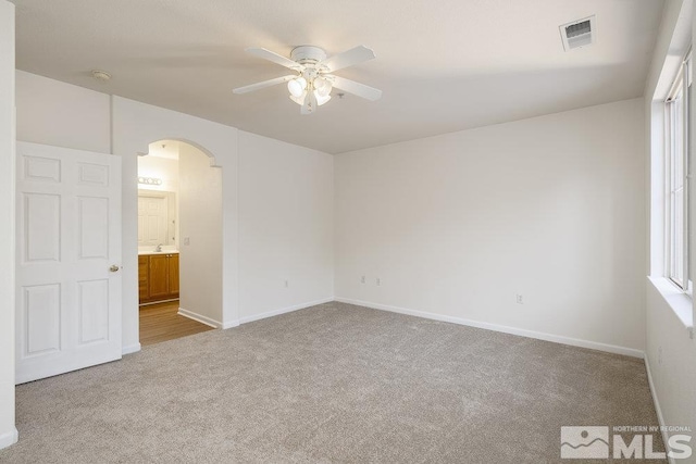 empty room featuring baseboards, visible vents, carpet floors, arched walkways, and ceiling fan