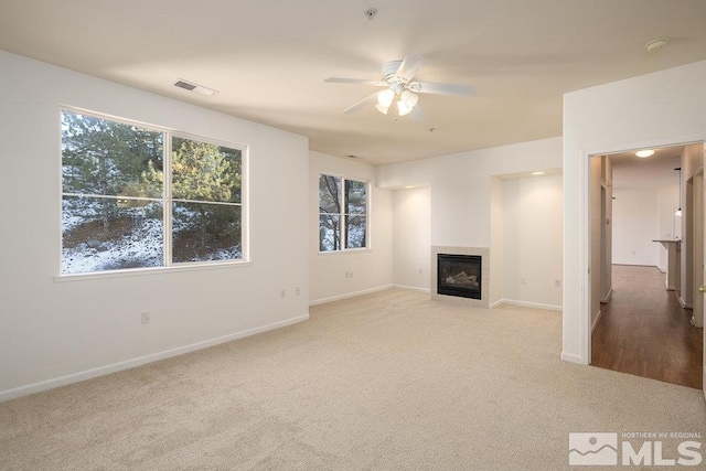 unfurnished living room with ceiling fan, light colored carpet, and a tiled fireplace