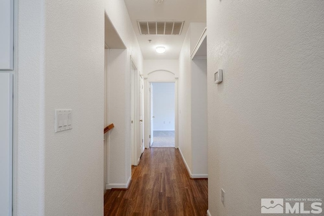 hallway with visible vents, baseboards, wood finished floors, and a textured wall