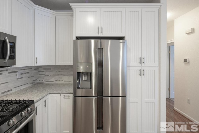 kitchen featuring backsplash, light stone countertops, wood finished floors, white cabinets, and stainless steel appliances