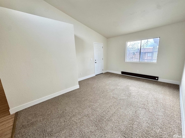 empty room featuring lofted ceiling, a baseboard heating unit, and carpet flooring