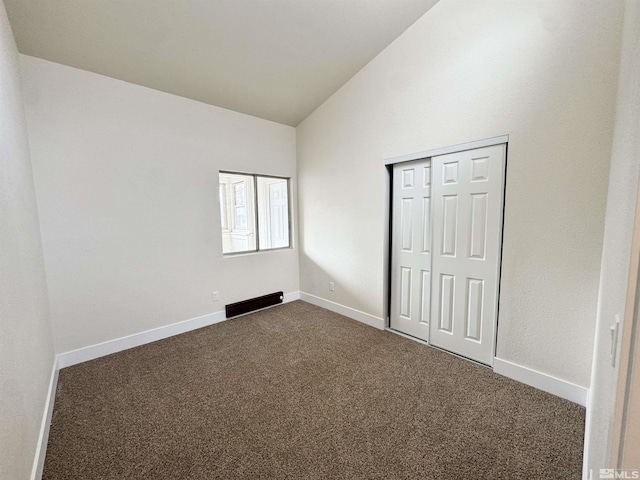 unfurnished bedroom with dark colored carpet, vaulted ceiling, and a closet