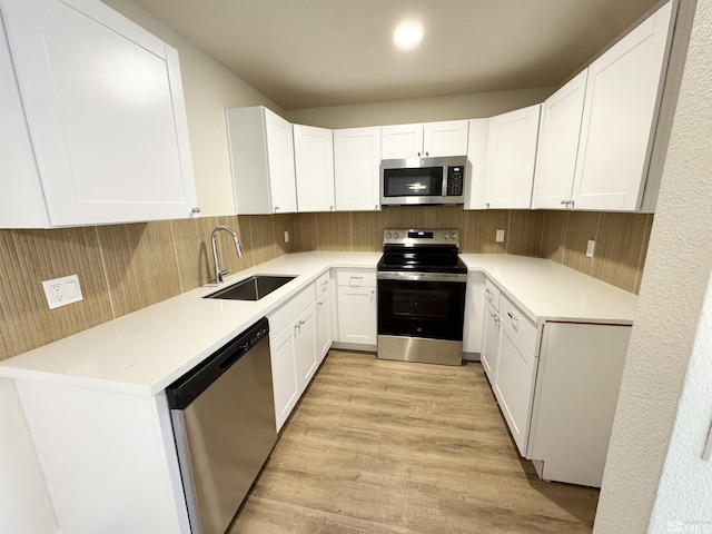 kitchen featuring appliances with stainless steel finishes, sink, white cabinets, backsplash, and light hardwood / wood-style flooring